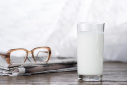 Milchglas steht auf Holzuntergrund vor Zeitung und Brille