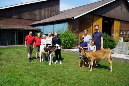Zwei Familien stehen auf einem Bauernhof und streicheln ein Kalb